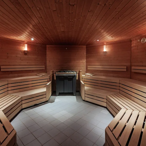 En tresauna med benker som omgir en sentral varmeapparat med steiner, opplyst av myke vegglamper som skaper en varm og innbydende atmosfære.