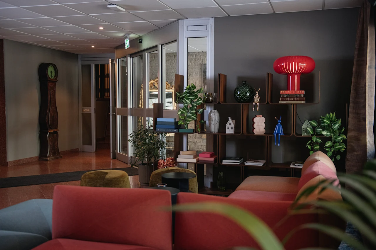 Et koselig salongområde med en rød sofa, en dekorativ hylle og glassdører som fører til en spisesal merket MATSAL.