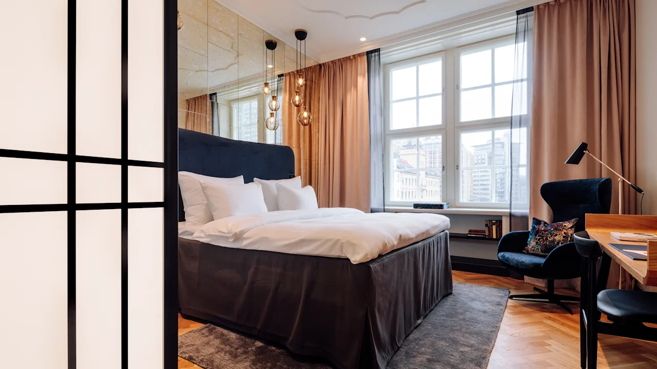Ett mysigt hotellrum med en stor säng, en bekväm fåtölj och ett skrivbord vid ett ljust fönster.