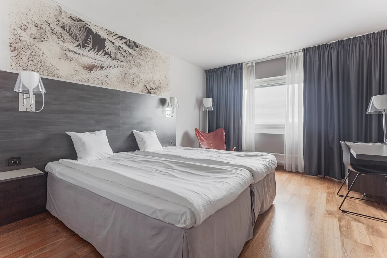 A welcoming hotel room with twin beds, a workspace, and a large window providing natural light.