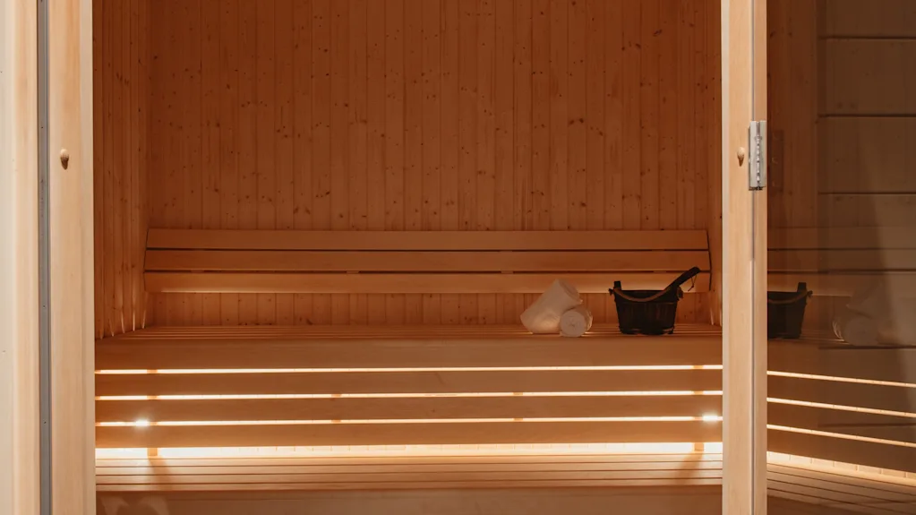 En varm, indbydende træsauna med bænke, en spand og håndklæder, klar til en afslappende oplevelse.