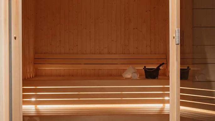 En varm, innbydende trebadstue med benker, en bøtte og håndklær, klar for en avslappende opplevelse.