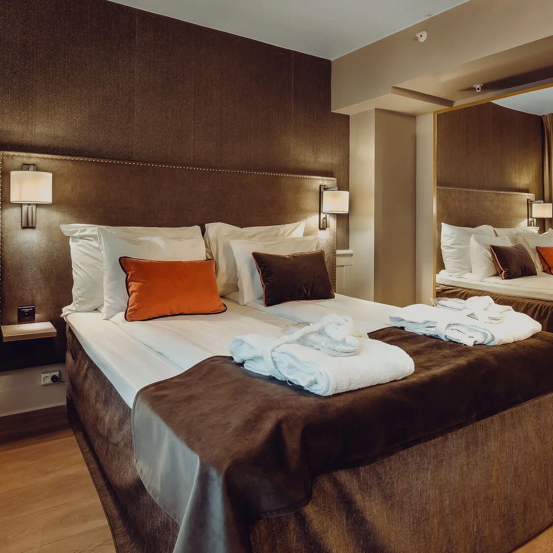 A neatly made bed with white linens, accented pillows, and towels in a well-lit hotel room.