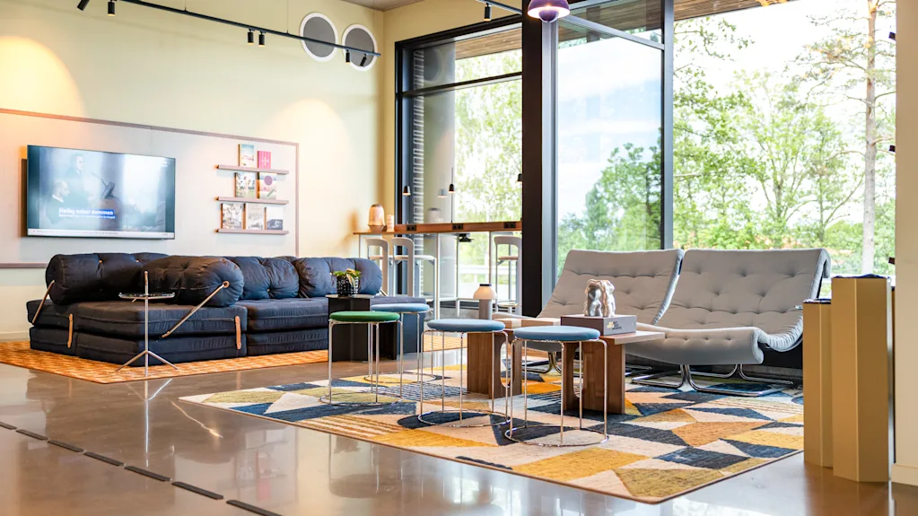 A modern and inviting lounge area with comfortable seating, a large TV, and big windows overlooking lush greenery.