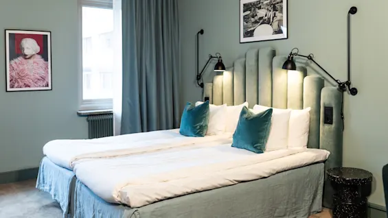 Et koselig hotellrom med to senger, myk belysning og beroligende grønne og blå toner, som inviterer til avslapning.