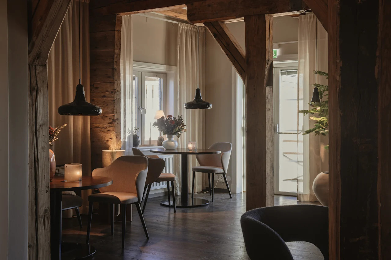 Et hyggeligt spise- eller loungeområde med rustikke træbjælker, borde, stole og blød belysning.