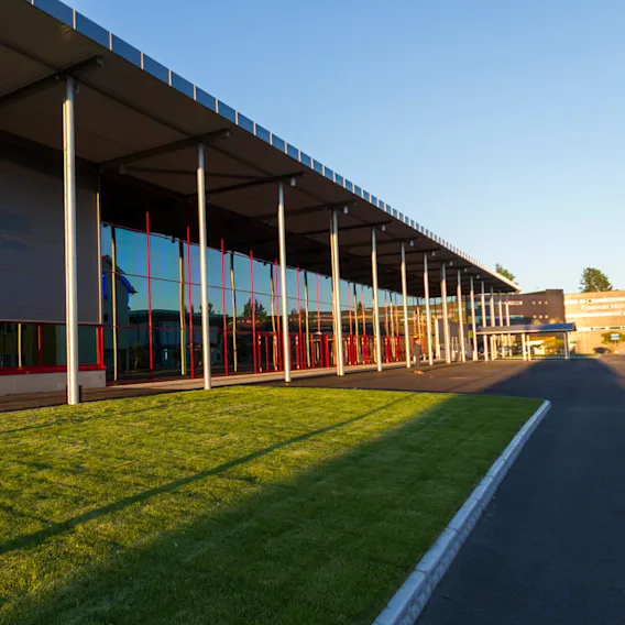 Building with large glass windows and metal poles reflecting sunlight in an airport setting. Text on building: "THE QUBE Clarion Hotel & Congress Oslo Airport."