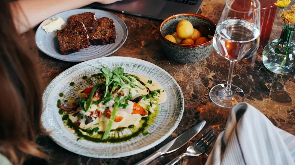 Person äter: en tallrik med sallad, bröd och en bärbar dator på ett marmorbord med ett glas vatten och vin.