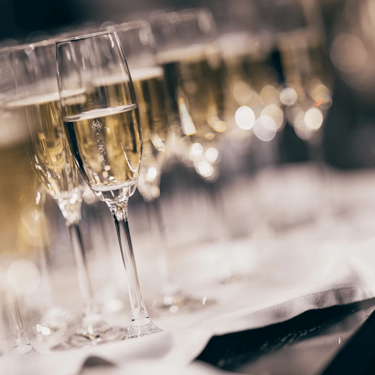 Champagneglass fylt med boblende væske er på rekke og rad på et bord dekket med hvit duk, og skaper en elegant og festlig atmosfære.
