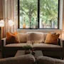 A cozy lounge area with a sofa, warm lighting, and lush greenery visible through a large window, creating an inviting atmosphere.