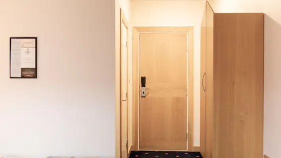 En ren og funksjonell hotellromsinngang med en tredør, en garderobe og en innrammet informasjonstavle.