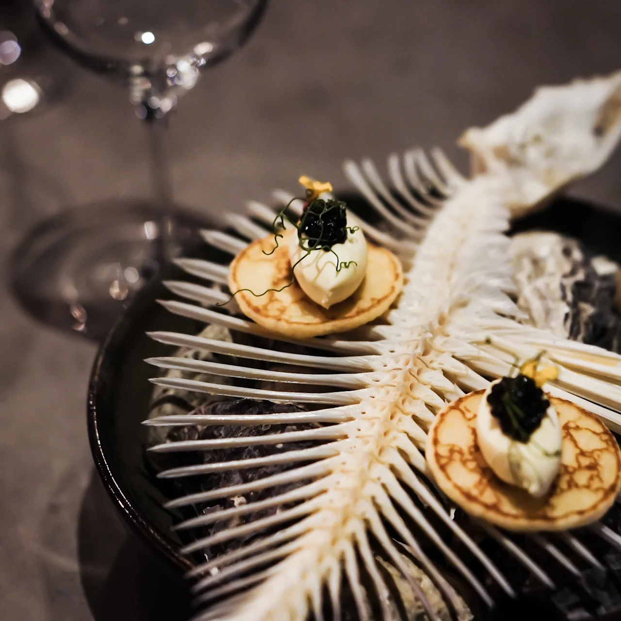 Tyylikkäät blinit kerman ja kaviaarin kera, tarjoiltuna taidokkaalla kalan luurakenteella, viinilasin ollessa lähellä.