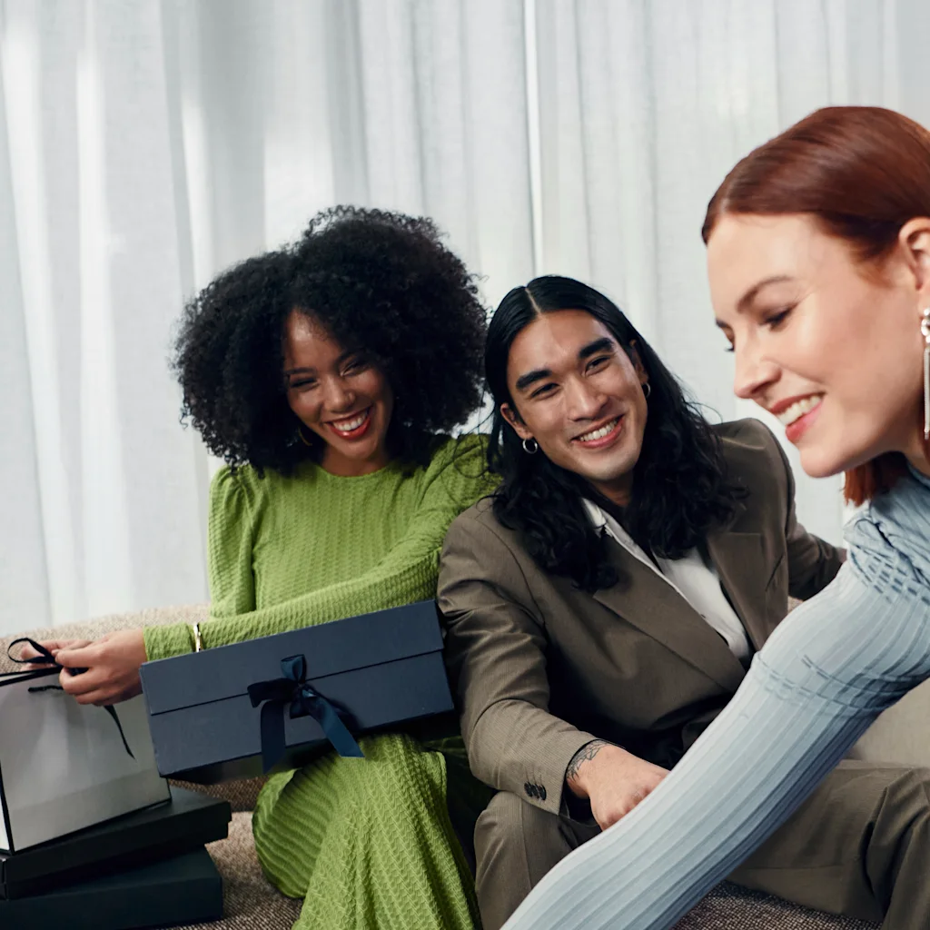 Tre smilende personer samlet rundt gaveesker og en handlepose, nyter et øyeblikk av delt glede.