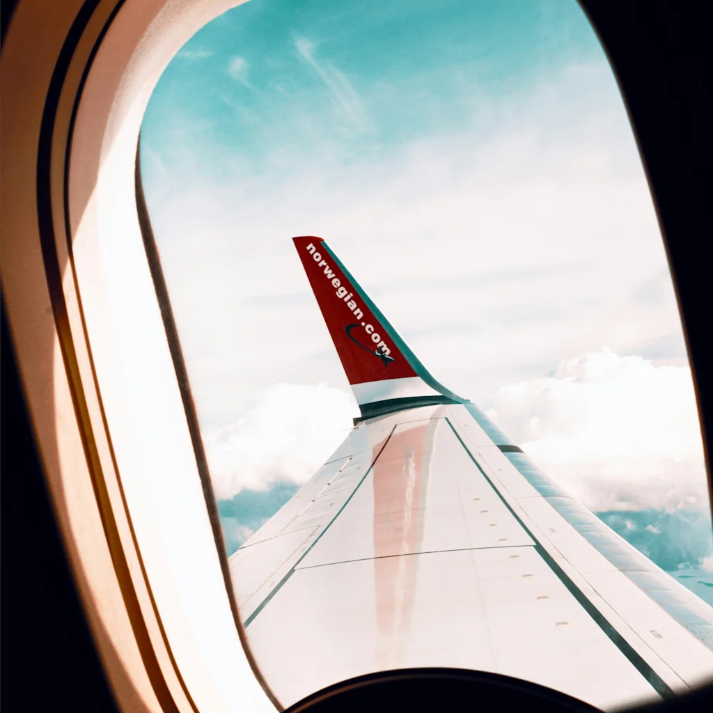Utsikt från ett flygplansfönster som visar vingen, moln och blå himmel. Text S 0216 224 syns på fönsterkarmen.