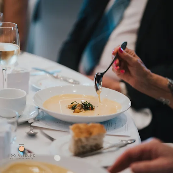 Nærbilde av en gjest som spiser en kremet suppe toppet med krutonger og urter ved et bryllupsbord.
