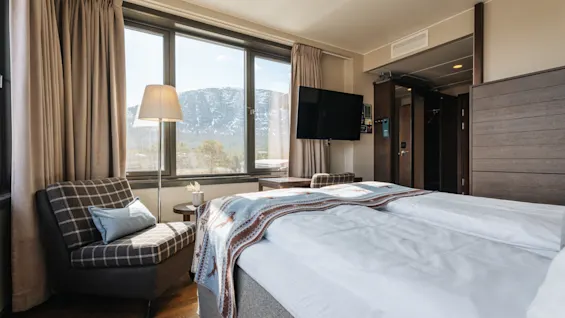 Ljust hotellrum med en stor säng, en fåtölj vid fönstret och utsikt mot bergen utanför.