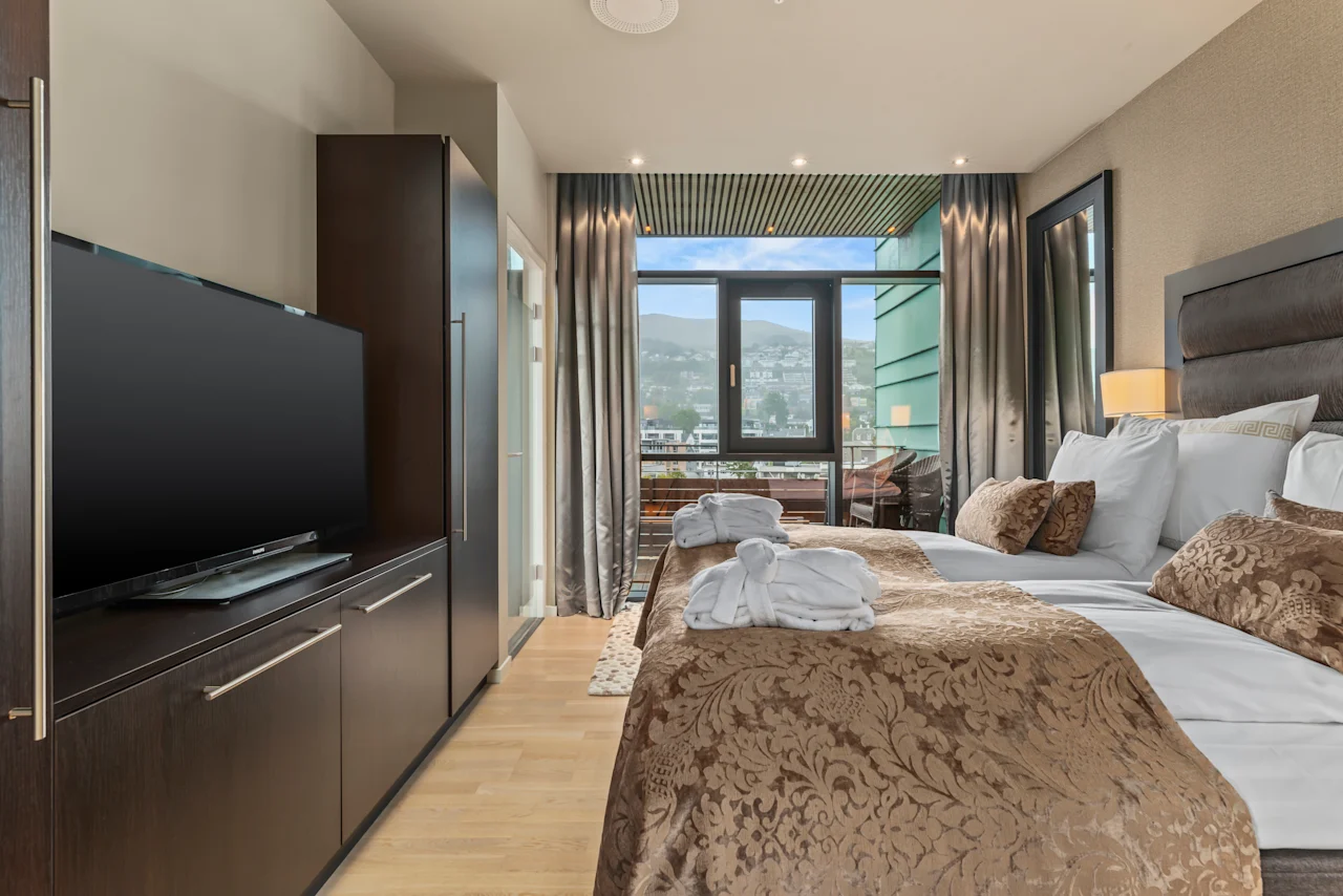 Et komfortabelt hotellrom på Quality Hotel Ulstein med to senger, en TV og en balkong som tilbyr en naturskjønn utsikt over byen.