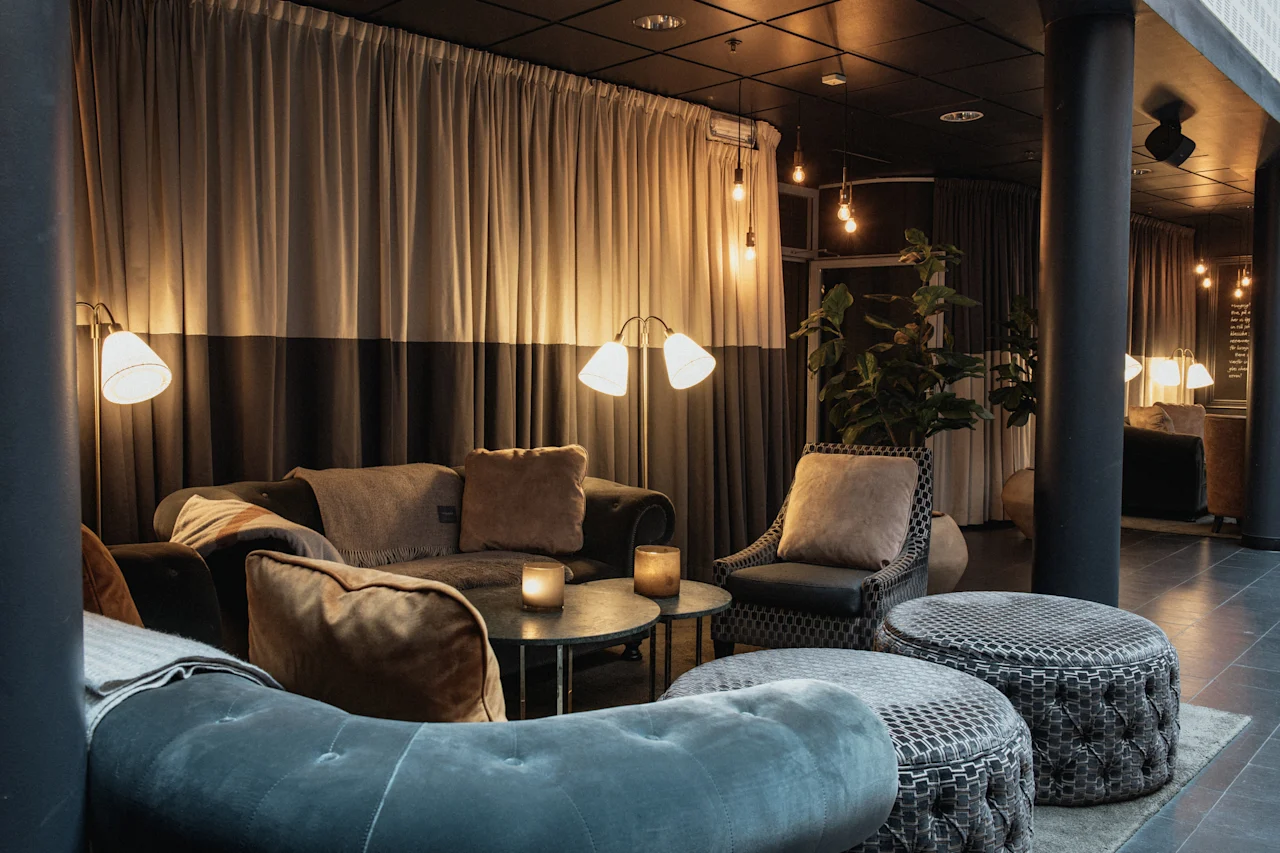 En varm og indbydende hotellounge med komfortable sofaer, lænestole og blød belysning, perfekt til afslapning.