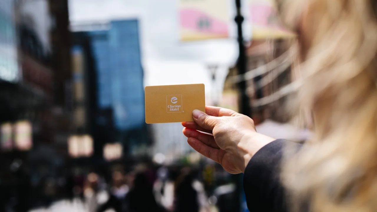A hand holds a golden hotel card against a blurred city background, suggesting travel or urban exploration.