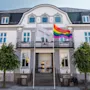 En indbydende hvid bygning med mørkt tag, der viser et hvidt flag med HOME TEL og et levende regnbueflag.