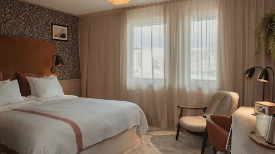 A cozy hotel room with a comfortable bed, a desk for work or relaxation, and a bright window letting in natural light.