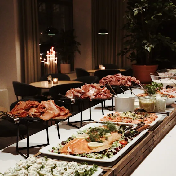 A Christmas buffet display featuring sliced salmon with lemon and dill, stuffed eggs, and cured meats on raised platters in a cozy restaurant setting.