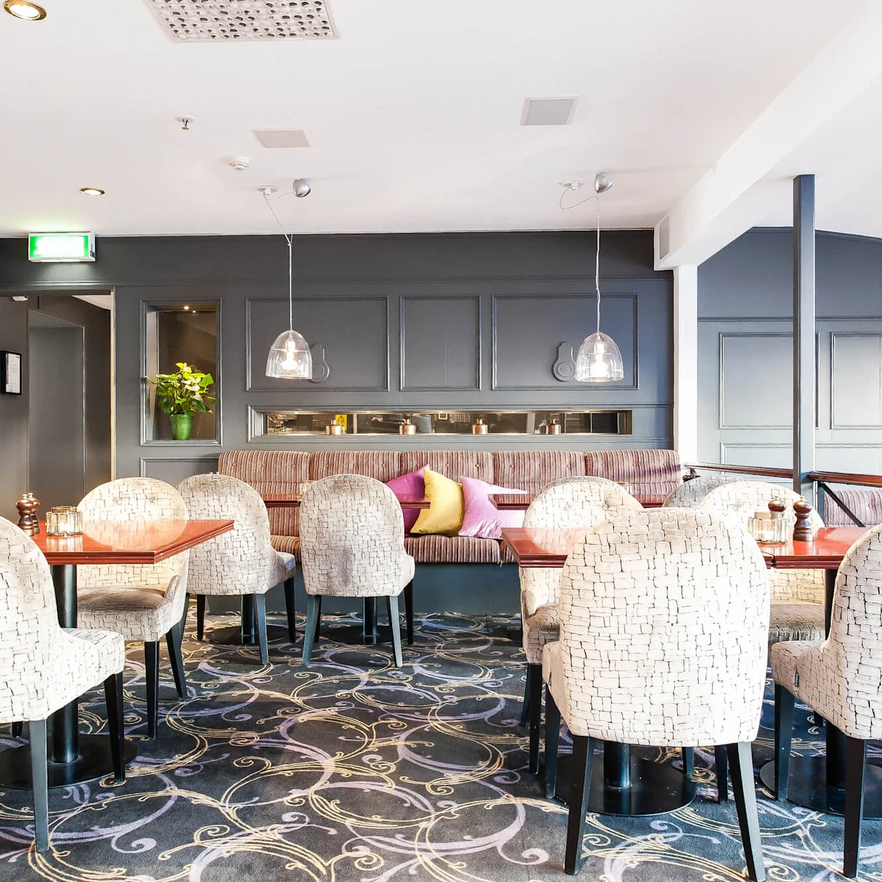 En elegant innredet restaurant med polstrede stoler, dekorativ belysning og en luksuriøs teppe i et innbydende rom uten kunder.