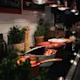 A kitchen counter with cooking pots, one holding sausages. Green plants and bottles are visible. Signs read TEAM SUITSPARKEN IN THE MOMENT.