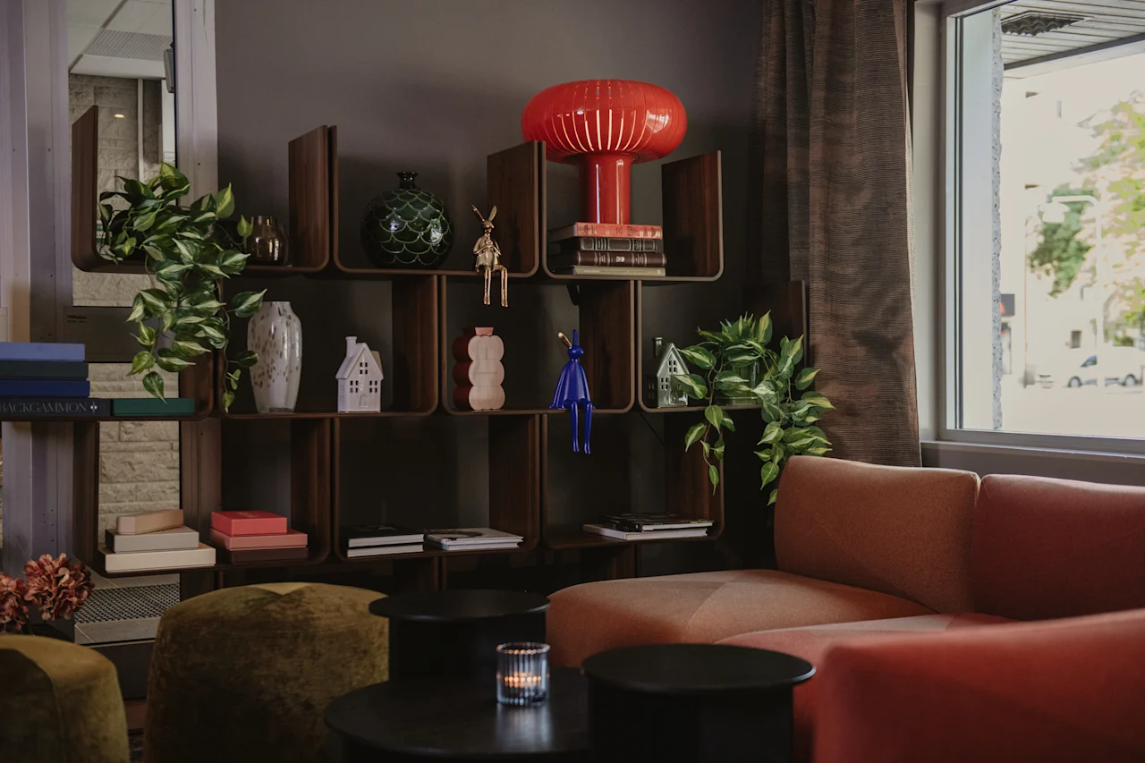 Et varmt og innbydende salongområde med en komfortabel sofa, dekorative hyller og naturlig lys fra et vindu.