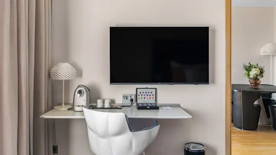 Et moderne hotelværelses skrivebordsområde med kaffemaskine, bærbar computer og vægmonteret TV, der tilbyder en behagelig arbejdsplads.