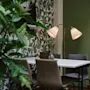Vitt bord med beige stolar, upplyst av en lampa med två skärmar, i ett rum med gröna väggar och bladig tapet; en växt syns i förgrunden.