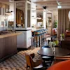 Moderne restaurantinteriør med en buffetskranke, der viser mad. Runde borde omgivet af røde polstrede sæder, midt i geometriske gulvfliser og pendelbelysning i en varmt oplyst atmosfære.