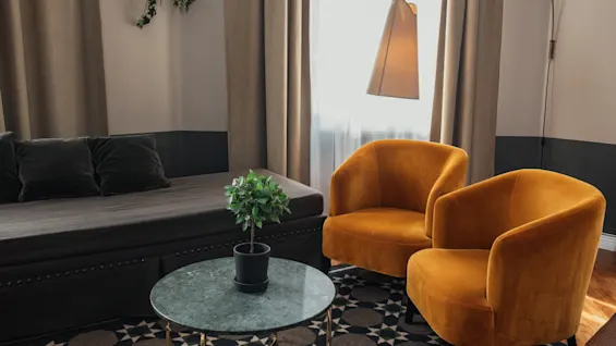 Et hyggeligt og indbydende opholdsrum med en daybed, to sennepsgule lænestole, et marmorsoffebord og et mønstret tæppe.