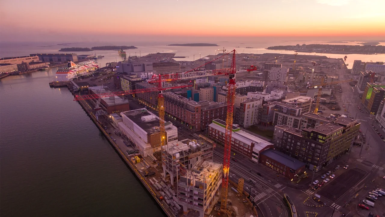 Ilmakuva kaupungin satamasta auringonlaskun tai -nousun aikaan, rakennuksia, rakennusnostureita ja telakoitu alus.