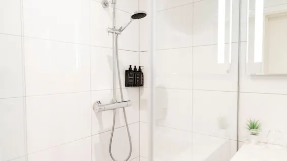 A bright and inviting shower space with white tiles, a modern shower fixture, and complimentary toiletries. Home Hotel Grand Bodø.