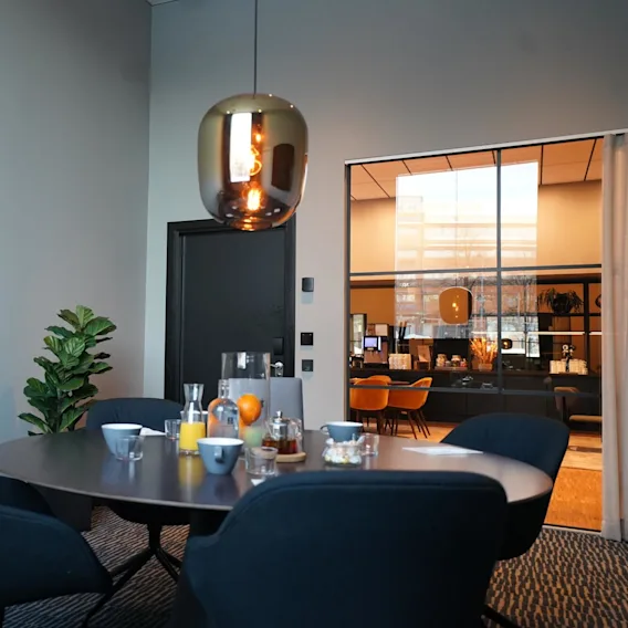 Dining table set with breakfast items, including juice and fruit, in a modern room with a hanging lamp and a visible interior through glass doors.