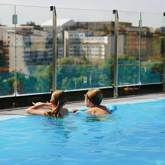 Two children enjoying a swim in a rooftop pool looking out at the city view