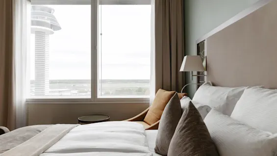 Ett inbjudande hotellrum med en bekväm säng och ett stort fönster med utsikt över ett modernt torn och det avlägsna landskapet.