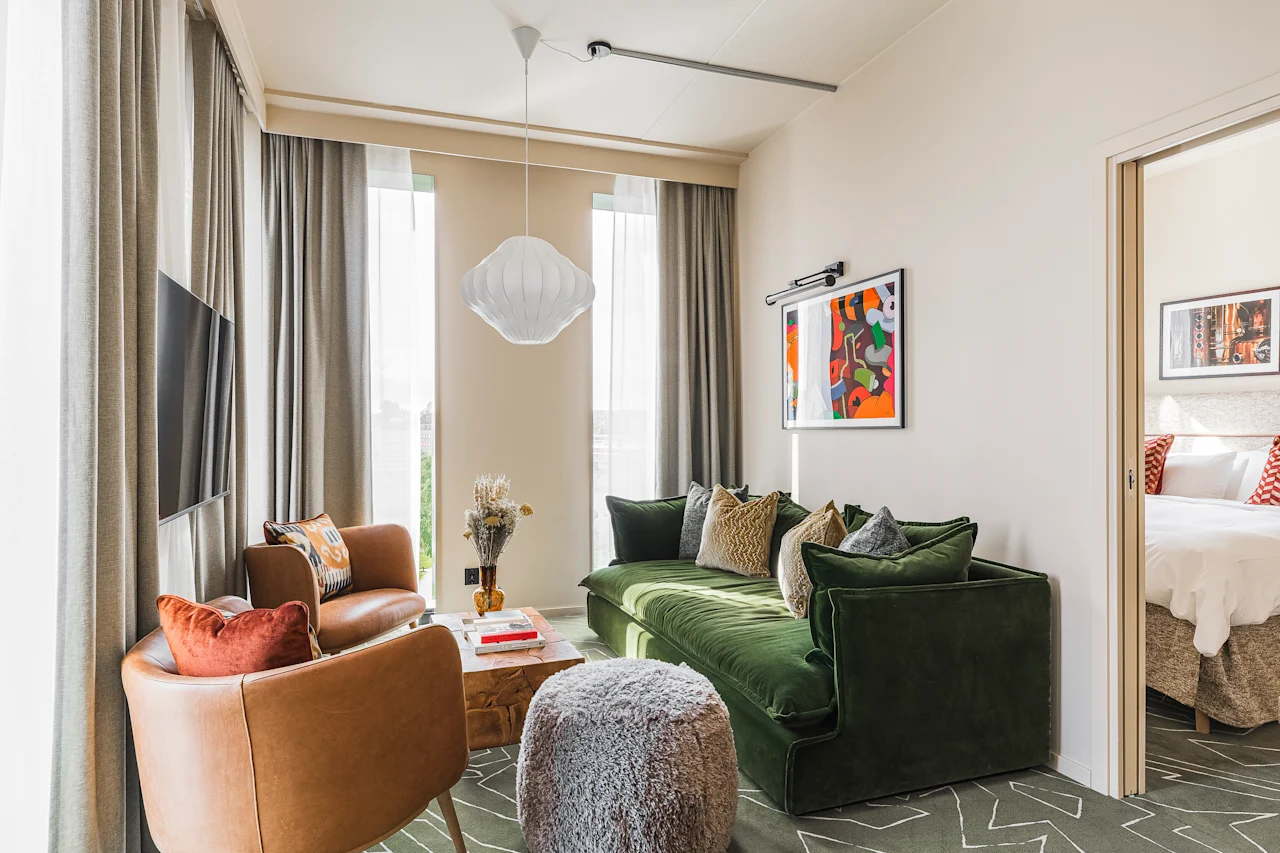 Et stilfuldt hotelsuite-opholdsrum på Hernö Gin Hotel, med en komfortabel grøn sofa, lænestole og et tilstødende soveværelse.