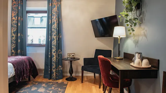 A cozy hotel room with a bed, a desk area, and a TV, featuring stylish decor. Home Hotel Kung Oscar.