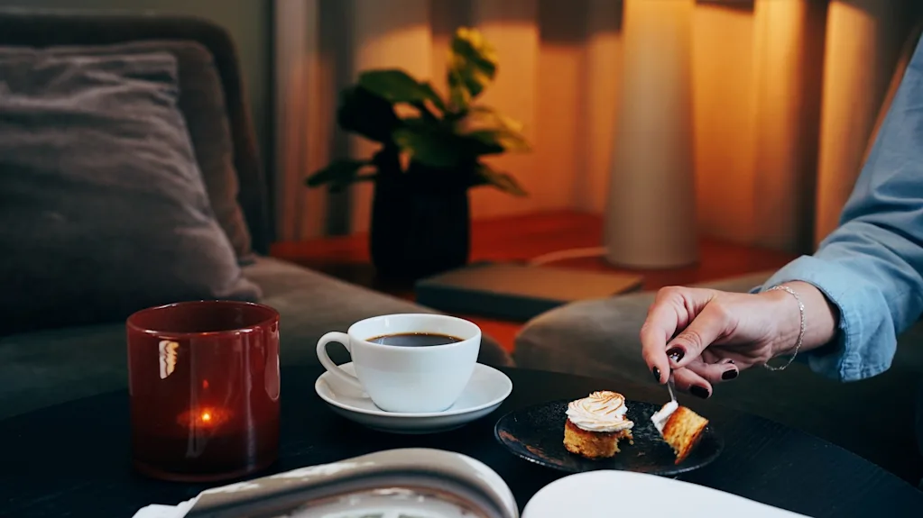 En person som koser seg med kaffe og kake i en koselig stue med tent lys.