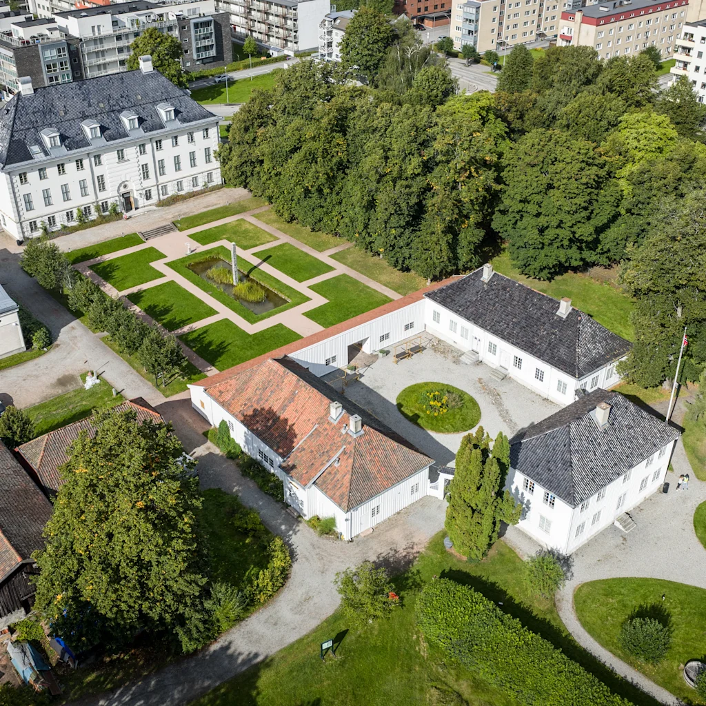 Flygfoto över en historisk vit herrgård med välskötta trädgårdar och omgivande grönska.