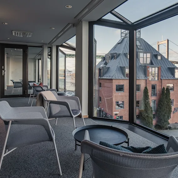 Ljus hotellounge med moderna stolar och stora fönster som erbjuder utsikt över en röd tegelbyggnad och en bro.