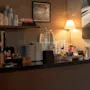 En indbydende selvbetjeningsstation med drikkevarer, kopper og tallerkener, oplyst af en varm lampe. Synlig tekst: SUGAR, TEA, COFFEE, N1.
