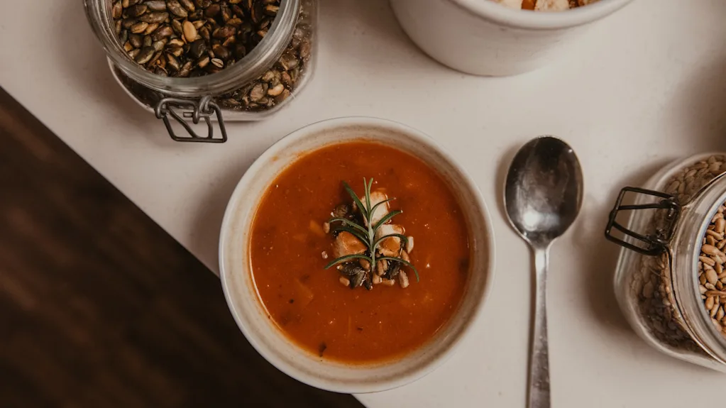 En varm skål suppe, garneret med friske urter og frø, klar til at blive nydt med en ske og diverse toppings.