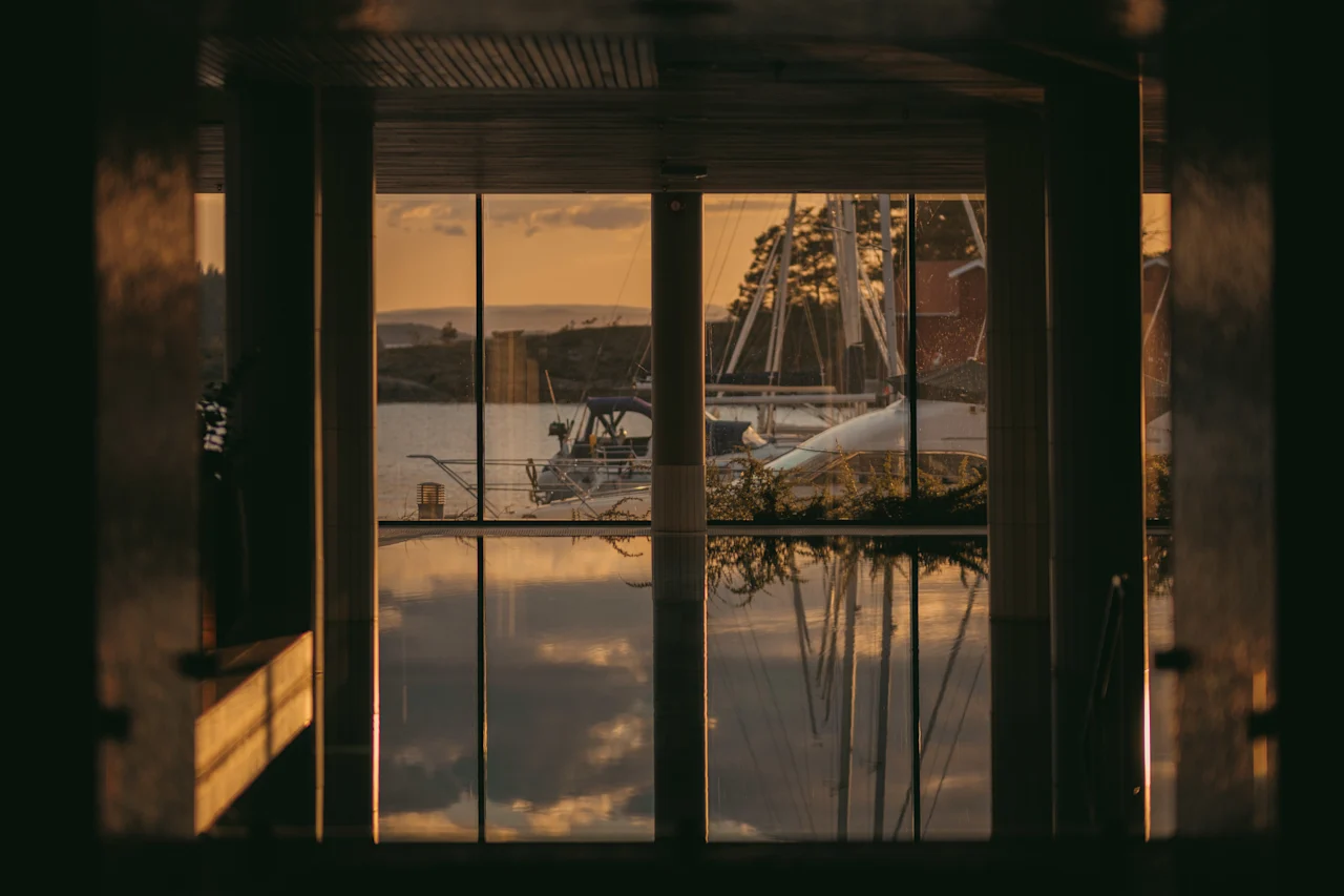 Gylden time lyser en rolig scene op med både på vandet, set fra et vindue, med refleksioner der danser på overfladen.