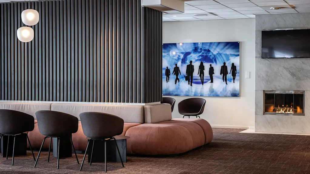 A seating area features modern chairs and a sofa facing a wooden panel. A digital artwork depicting silhouettes and a globe adorns the wall beside a lit fireplace.
