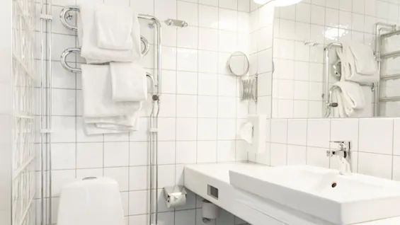 Ett rent, modernt badrum med vitt kakel, en toalett, ett handfat och fräscha vita handdukar på en handdukstork.