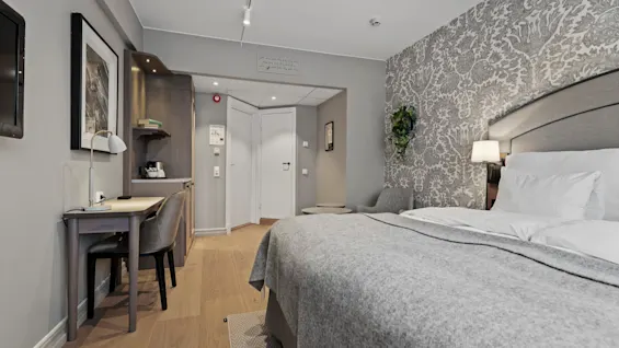 A comfortable hotel room with a large bed, a dedicated workspace, and stylish grey decor, ideal for rest and productivity.