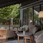A cozy outdoor patio with comfortable seating and tables, surrounded by greenery, perfect for relaxation.
